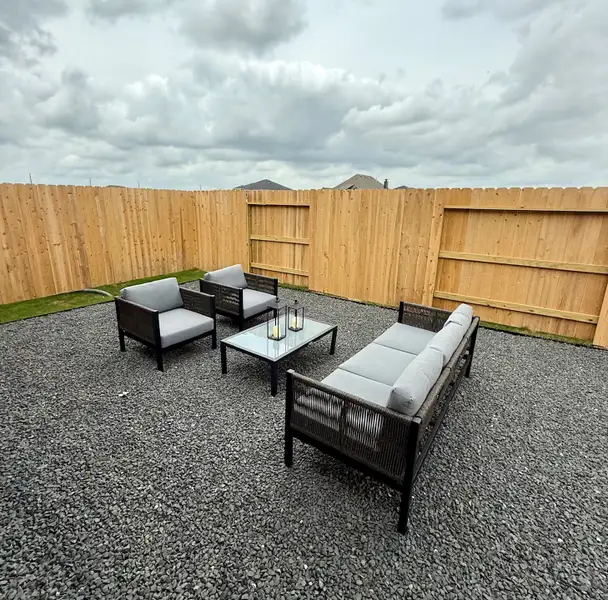 A minimalist outdoor space with sleek furniture, gravel flooring, and a wooden fence under a cloudy sky. A minimalist outdoor space with sleek furniture, gravel flooring, and a wooden fence under a cloudy sky.