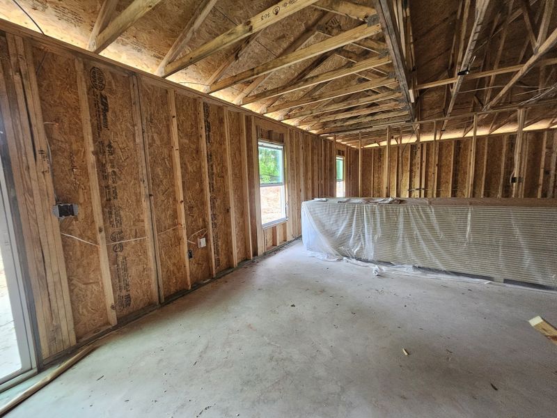 A framed interior under construction with exposed wooden beams and plastic-covered building materials on the floor.