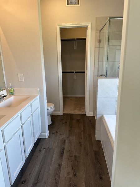 A modern bathroom with wood flooring, dual sinks, and a glass-enclosed shower next to a spacious walk-in closet.