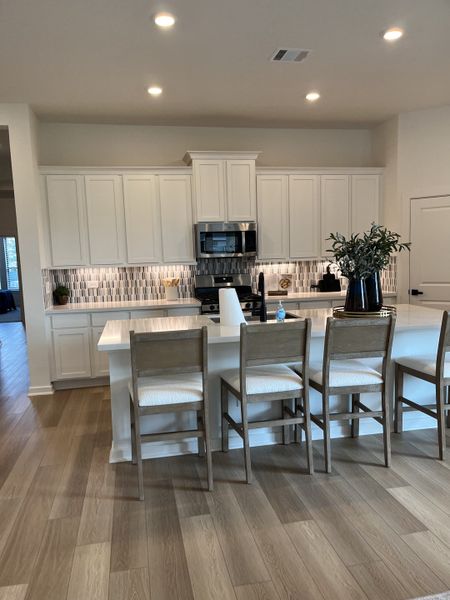 A modern kitchen with white cabinets, wood flooring, and a spacious island featuring stylish bar seating. A modern kitchen with white cabinets, wood flooring, and a spacious island featuring stylish bar seating.