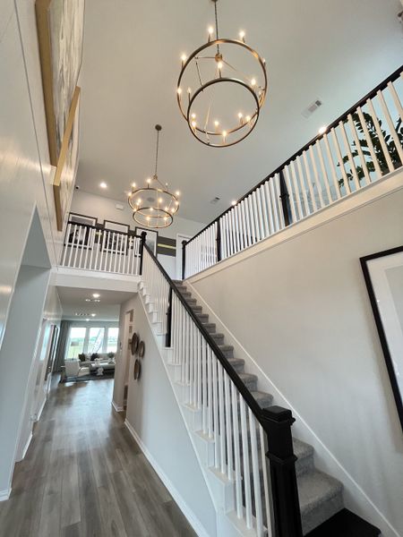 A grand foyer with elegant chandeliers, a white staircase, and sleek hardwood floors.