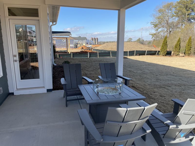 A cozy patio with Adirondack chairs and a fire pit table, offering a serene view of the spacious backyard.