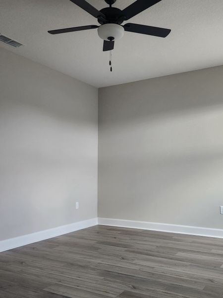 A modern bedroom with sleek gray walls, wood-style flooring, and a ceiling fan enhances comfort and style.