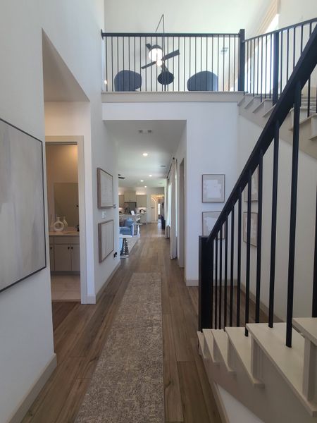 A spacious hallway with hardwood floors, modern railing, and an upstairs loft, exuding elegance and open design.