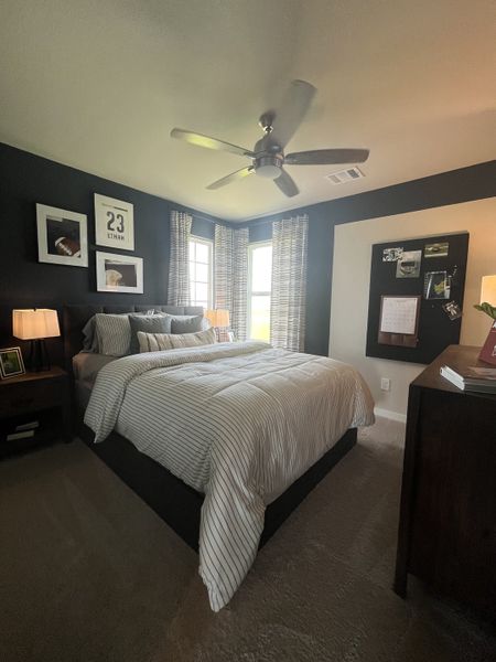 Cozy bedroom with a dark accent wall, striped bedding, ceiling fan, and soft carpet flooring. Cozy bedroom with a dark accent wall, striped bedding, ceiling fan, and soft carpet flooring.