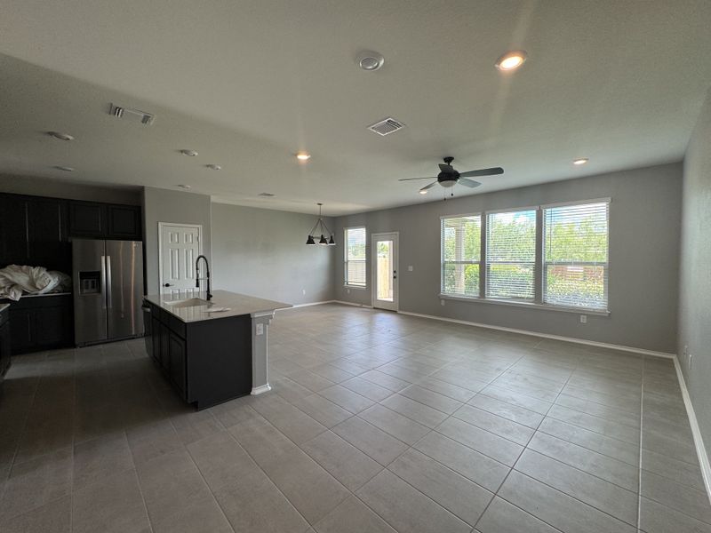 An open-concept living space featuring large windows, tile flooring, and a modern kitchen with dark cabinets and a sleek island.