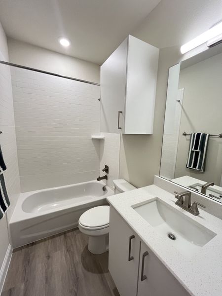 A modern bathroom with sleek white cabinets, a tiled bathtub, and wood-style flooring.