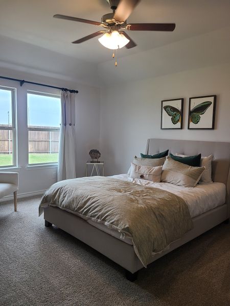 A cozy bedroom featuring a modern ceiling fan, soft carpeting, and elegant butterfly artwork on the walls.