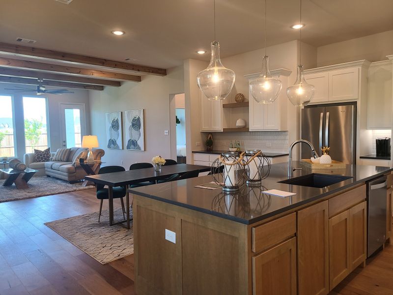 A modern open-concept kitchen and living area with wood beams, pendant lighting, and sleek furnishings.
