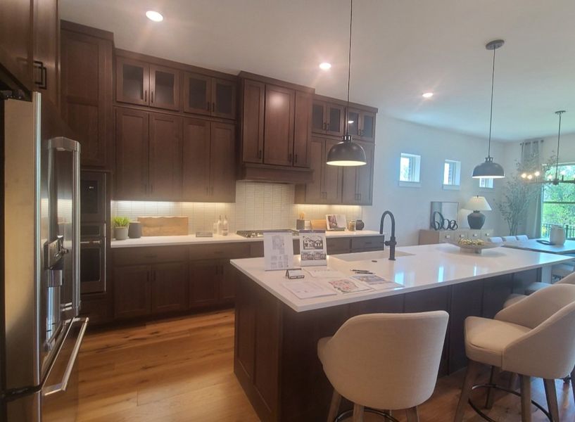 A modern kitchen with dark wood cabinets, white countertops, pendant lighting, and a spacious island with seating. A modern kitchen with dark wood cabinets, white countertops, pendant lighting, and a spacious island with seating.