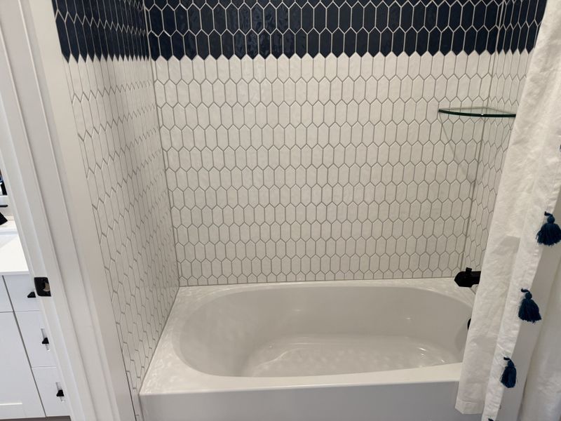 A modern bathroom with hexagonal tiled walls and a sleek white bathtub.