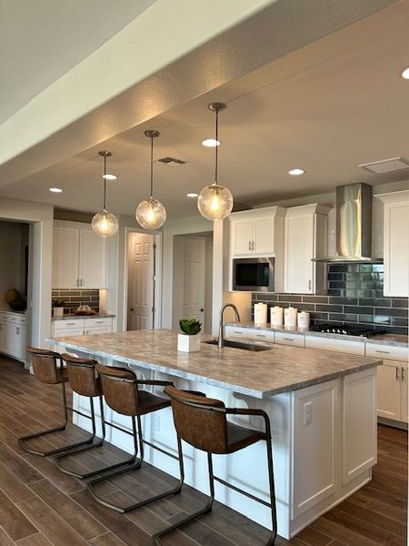 A modern kitchen featuring a large island, pendant lights, and sleek cabinetry with stainless steel appliances.