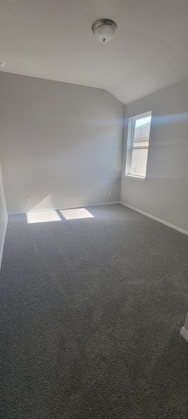 A bright, cozy room with soft gray carpeting, neutral walls, and a ceiling light fixture. Perfect for a home office or bedroom.