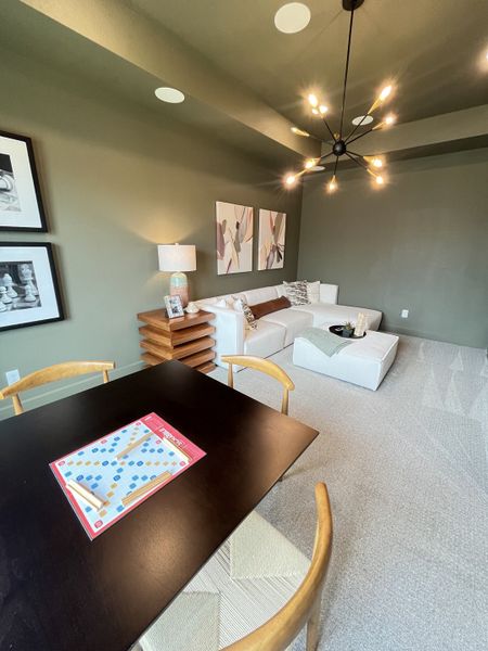 A cozy living area with a modern chandelier, comfy sectional, artistic decor, and a game-ready table.