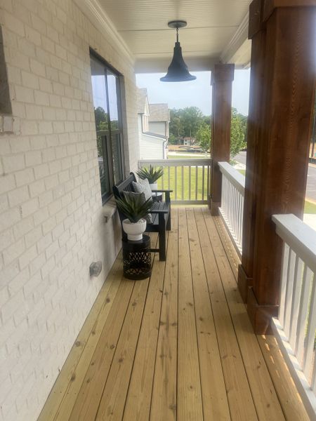 A cozy porch with wood floor, white brick wall, black lighting, and seating with planters for relaxation. A cozy porch with wood floor, white brick wall, black lighting, and seating with planters for relaxation.