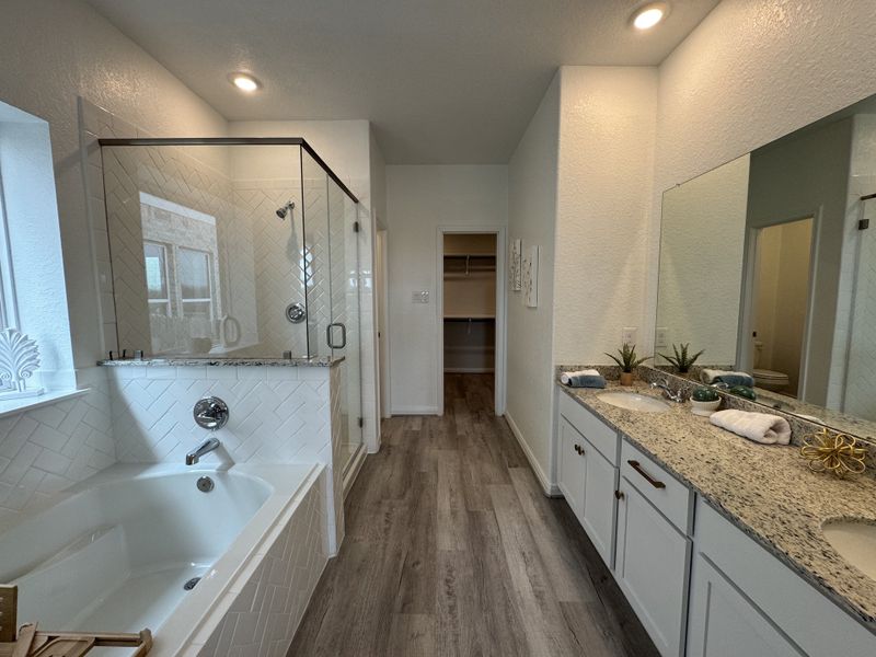 A modern bathroom with a glass shower, spacious tub, and dual-sink vanity featuring granite countertops and wood flooring.