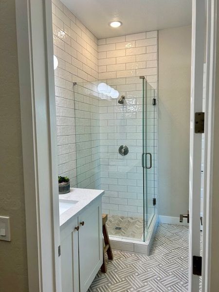 A modern bathroom with a glass-enclosed shower, white subway tiles, and chic geometric flooring.