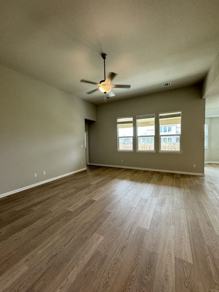 A spacious living area with wood flooring, neutral walls, and a ceiling fan for a modern, airy feel.