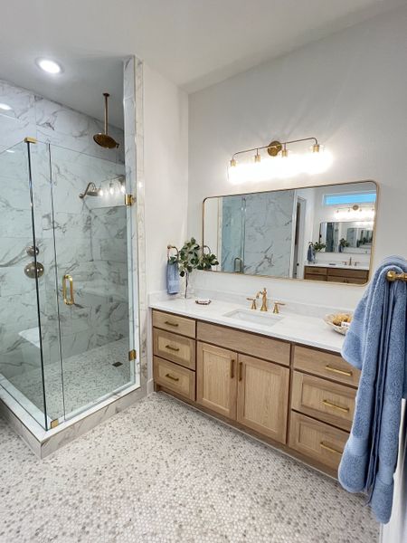 A modern bathroom featuring a marble shower, oak vanity, and elegant lighting with gold accents. A modern bathroom featuring a marble shower, oak vanity, and elegant lighting with gold accents.