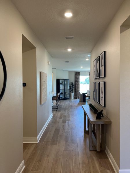A modern hallway with wood flooring, recessed lighting, and elegant wall art leading to a bright living area.