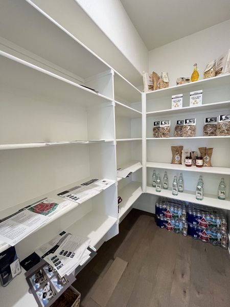 A spacious walk-in pantry with white shelving, organized with snacks, bottles, and kitchen essentials.