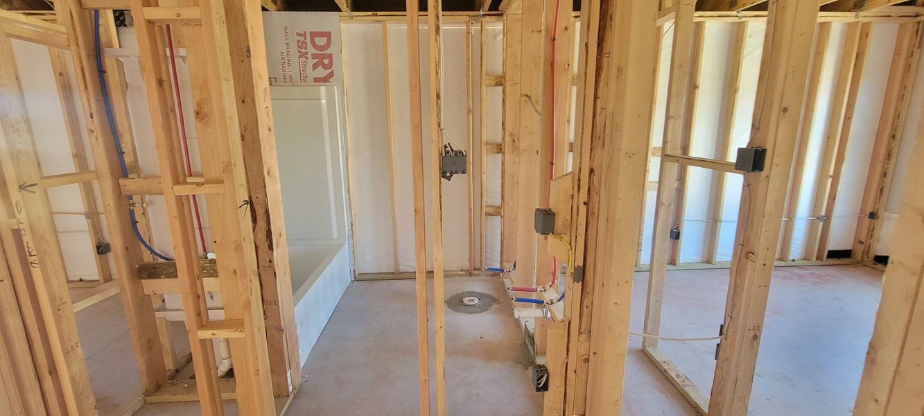 A house under construction with exposed wooden framing and plumbing installation visible.