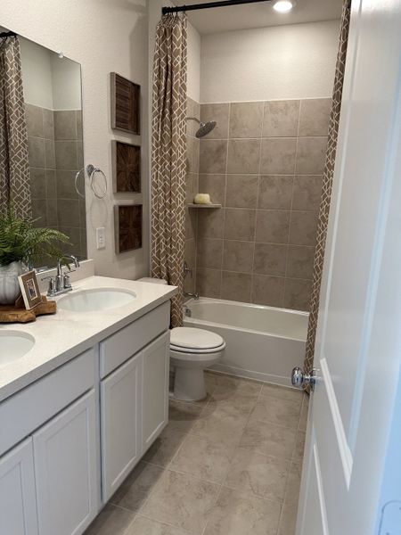 A modern bathroom featuring dual sinks, beige tiled shower, and geometric-patterned curtains. A modern bathroom featuring dual sinks, beige tiled shower, and geometric-patterned curtains.