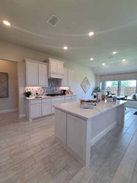 A spacious kitchen with white cabinetry, modern backsplash, and a large island, featuring sleek recessed lighting.