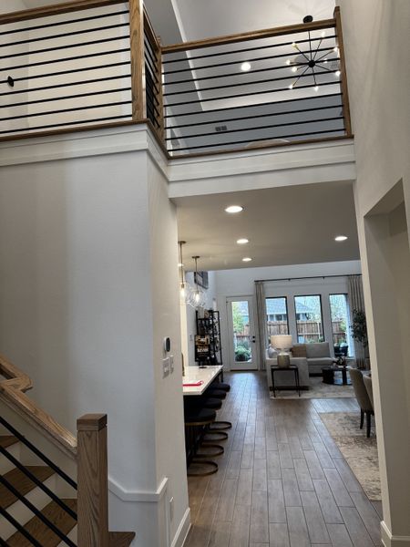 A modern open-concept living area with high ceilings, sleek railing, and wood floors, leading to a cozy, light-filled lounge. A modern open-concept living area with high ceilings, sleek railing, and wood floors, leading to a cozy, light-filled lounge.