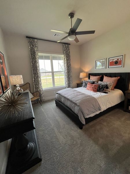A cozy bedroom with a modern ceiling fan, chic decor, and large window draped with patterned curtains. 