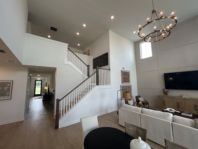 A spacious living area with high ceilings, modern chandelier, and elegant staircase, perfect for open-concept living.