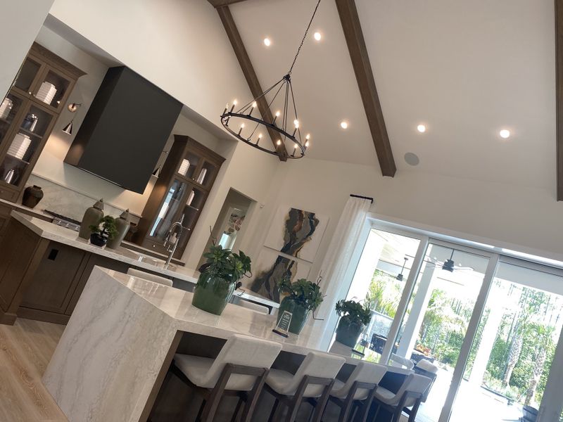 A modern kitchen with a marble island, elegant pendant lighting, and large windows opening to lush greenery.