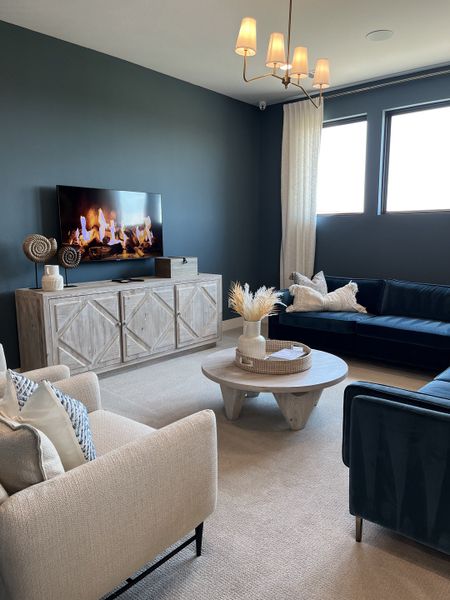 A cozy living room featuring a blue accent wall, comfortable seating, a wooden media console, and elegant lighting.