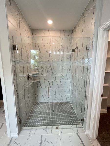 A modern shower with elegant marble-patterned tiles, glass door, and sleek fixtures for a luxurious bathing experience.