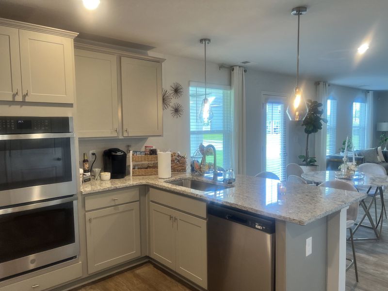 A modern kitchen with granite countertops, stainless steel appliances, and pendant lighting, opening into a bright dining area.