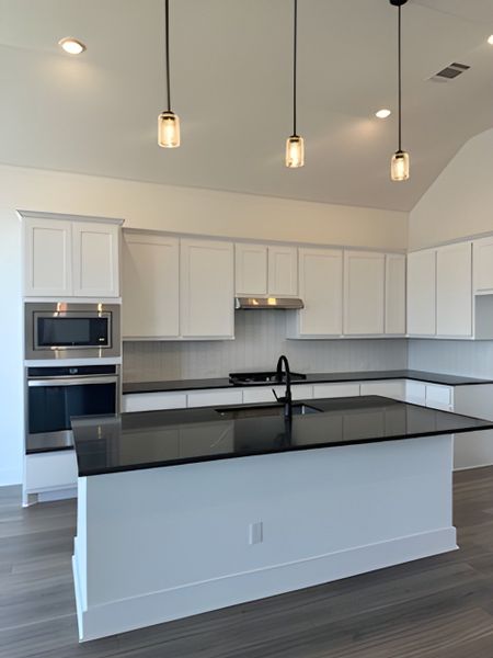 A modern kitchen with sleek black countertops, white cabinetry, stainless steel appliances, and stylish pendant lighting.