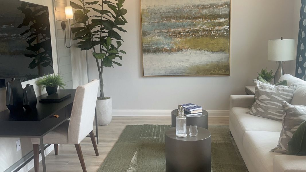 A cozy living area with modern art, a sleek desk, and a plush sofa, accented by a tall plant and stylish decor.