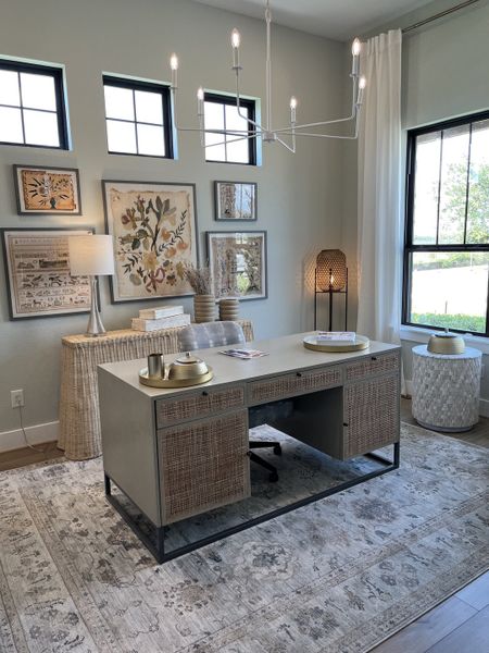 A chic home office with a modern desk, neutral decor, and nature-inspired artwork, complemented by large windows and elegant lighting.