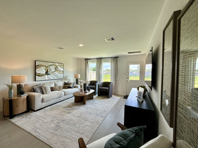 A cozy living room with a large sofa, abstract art, and ample natural light from wide windows and a door to a serene yard.