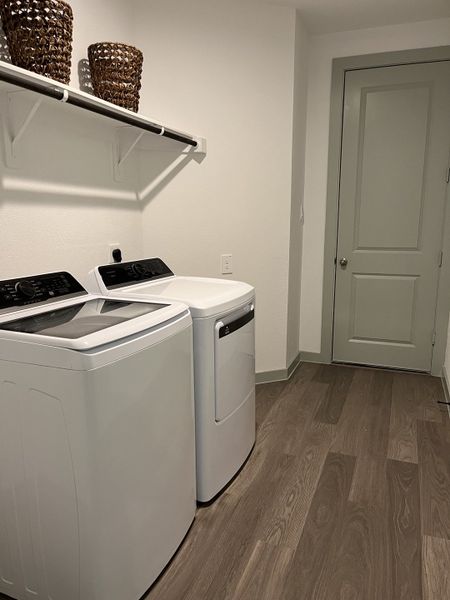 A sleek laundry room featuring modern appliances, wood-patterned flooring, and smart shelving with wicker baskets.