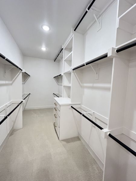 A spacious walk-in closet featuring ample shelving, hanging rods, and plush carpeting for a luxurious storage solution. A spacious walk-in closet featuring ample shelving, hanging rods, and plush carpeting for a luxurious storage solution.