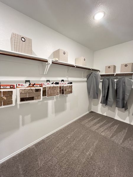 A spacious walk-in closet with neatly organized shelves, hanging suits, and soft carpet flooring.