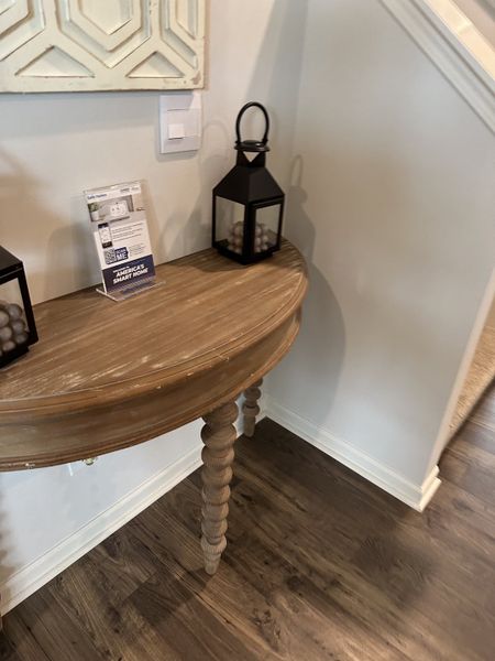 A cozy corner with a rustic half-moon table, black lantern decor, and elegant wooden floors.