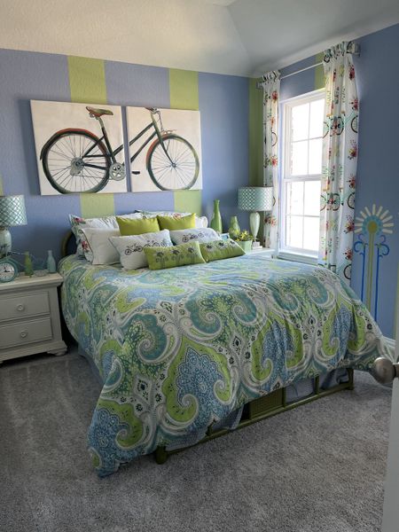 A vibrant bedroom with blue and green accents, bicycle artwork, and a paisley bedspread, creating a cozy, cheerful ambiance. A vibrant bedroom with blue and green accents, bicycle artwork, and a paisley bedspread, creating a cozy, cheerful ambiance.