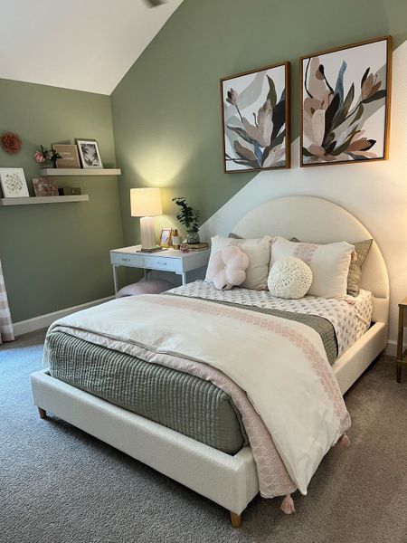 A cozy bedroom with a plush bed, green accent wall, and elegant decor, featuring botanical artwork and soft lighting.