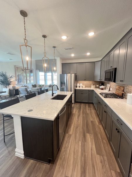 A modern kitchen featuring sleek gray cabinets, wooden floors, elegant lighting, and a spacious island with a marble countertop. A modern kitchen featuring sleek gray cabinets, wooden floors, elegant lighting, and a spacious island with a marble countertop.