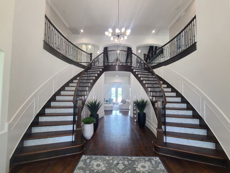 A grand foyer with a double curved staircase, elegant chandelier, and rich wood flooring. A grand foyer with a double curved staircase, elegant chandelier, and rich wood flooring.