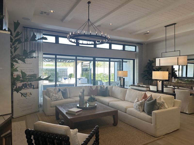 A bright living room featuring a cozy sectional, modern chandelier, and expansive windows opening to a patio.