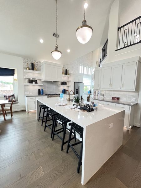 A modern kitchen with white cabinetry, spacious island, and sleek pendant lighting.