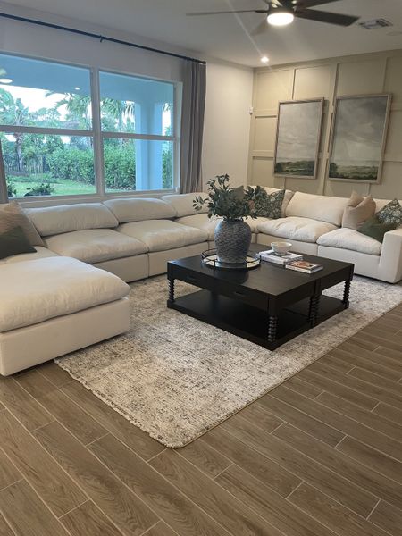 A cozy living room with a plush sectional, large windows, and a chic coffee table on a patterned rug.